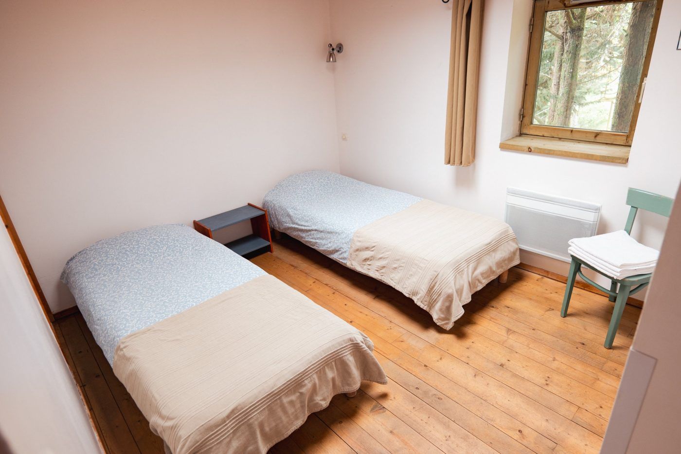 Bedroom with two single beds, wooden floor and a window opening onto the pines