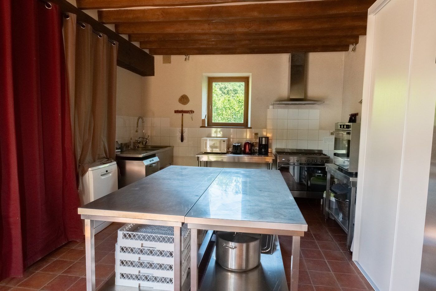La cuisine de la maison forestière : îlot inox central, piano de cuisson, plonge et poutres apparentes