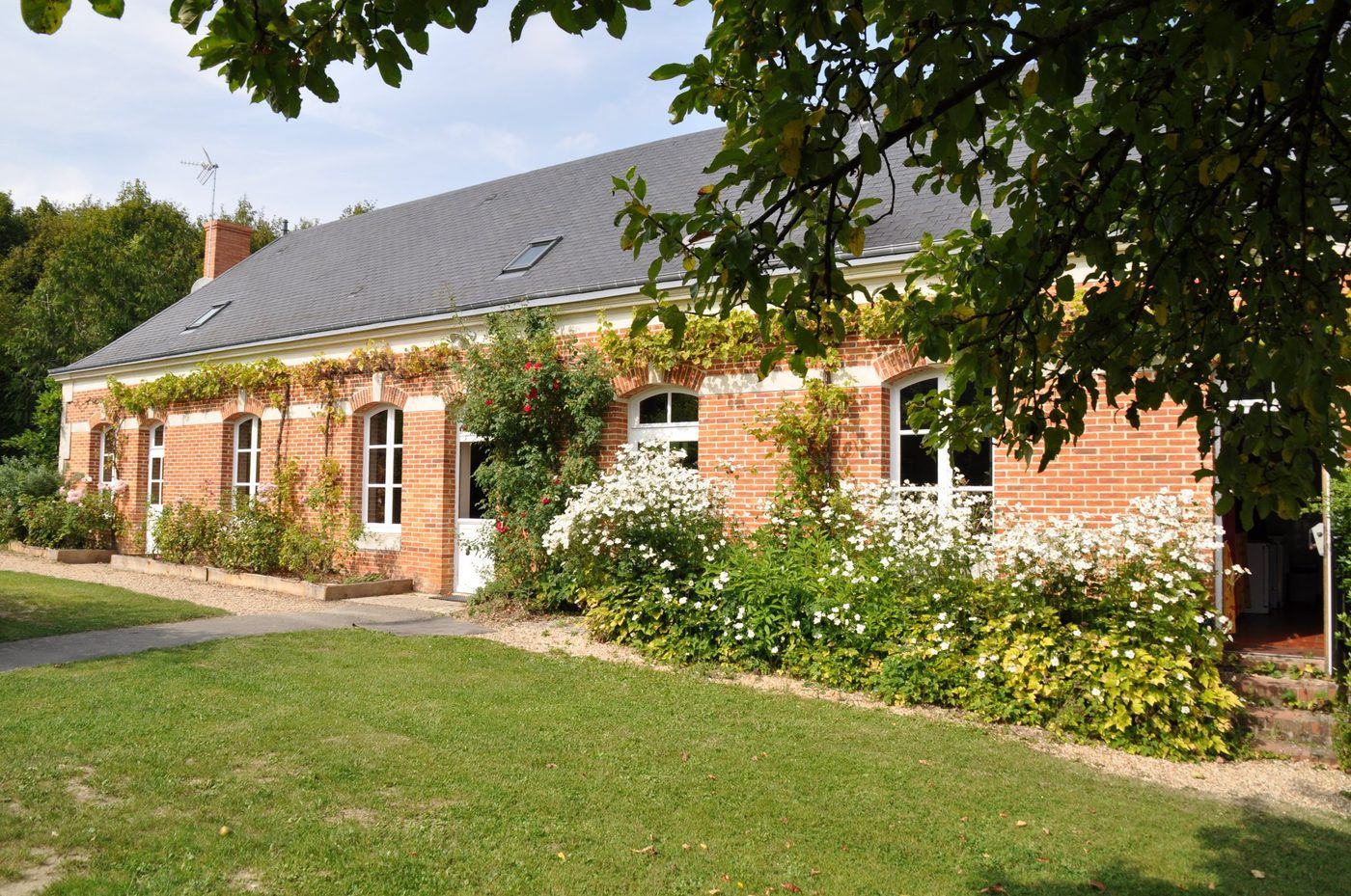 La maison forestière en briques, sa façade fleurie et ses fenêtres cintrées