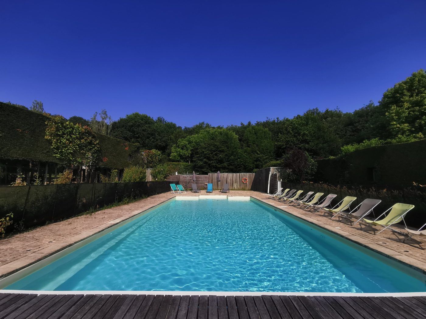 La piscine bordée de transats, entourée de murs végétaux et d’arbres
