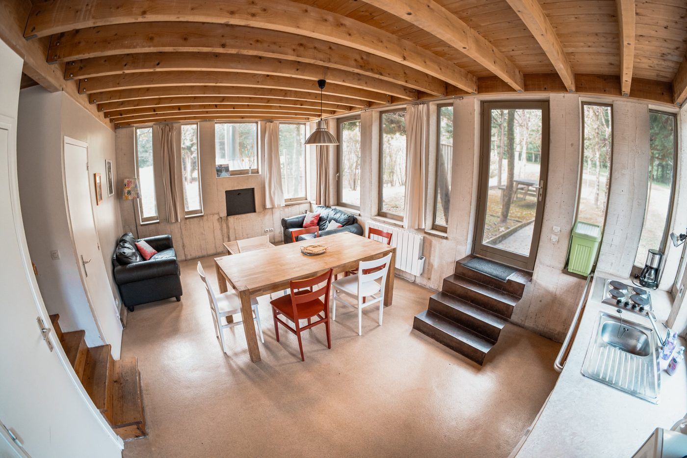 Living space in a chalet: timber beams, a large table and picture windows onto the trees
